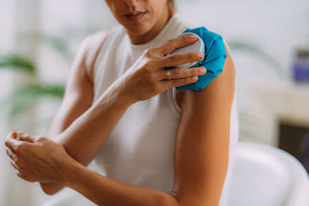 Frozen shoulder. Woman holding cold compress, ice bag pack on her painful shoulderの写真素材