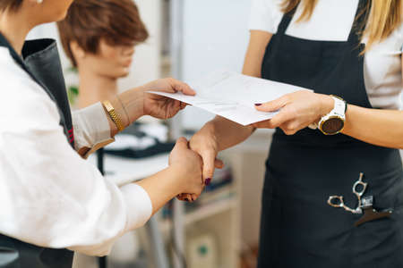 Hands of Hairdressing Educator Giving Hairstylist Certificate to a Student after Successfully...