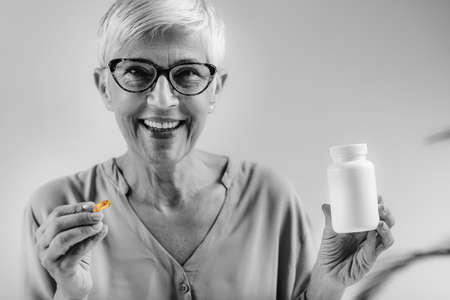 Senior woman holding Vitamin D Capsule and Bottle.の写真素材