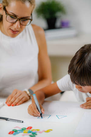 Child drawing shapes in a preschooler assessment test. Psychologist helping him.