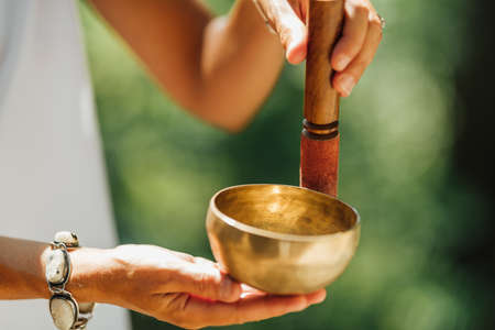 Hands holding Tibetan singing bowl outdoors, playing calming soundsの写真素材
