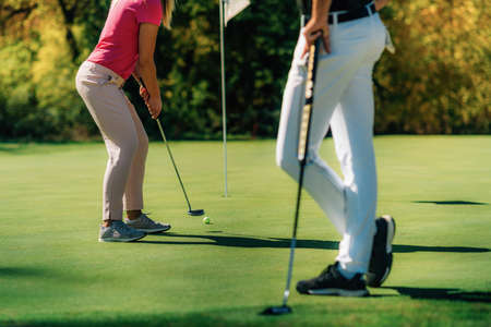 Golf couple putting on the green, unrecognizable peopleの写真素材