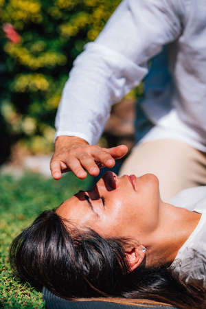 Close-up image of relaxed woman lying with her eyes closed and having Reiki healing treatment in nature. Energy healing concept.の写真素材
