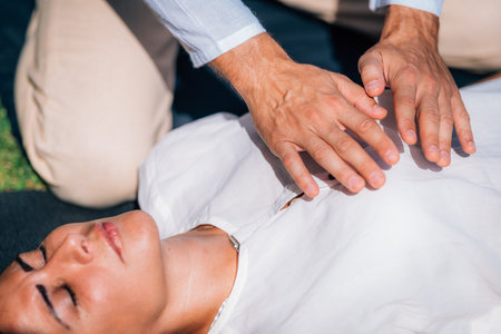 Woman in Reiki spiritual healing session. Reiki therapist holding hands above heart chakra and...