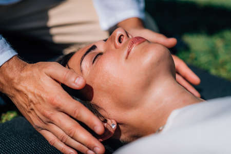 Woman in Reiki spiritual healing session. Reiki therapist holding hands above heart chakra and transferring energy. Peaceful woman is lying with her eyes closed.の写真素材