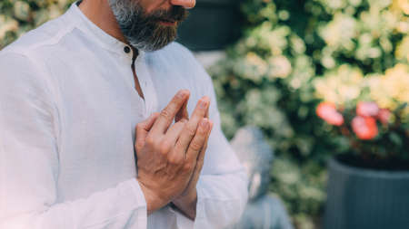 Gratefulness meditation. Peaceful man sitting in a lotus pose and meditating, keeping hands together in a prayer position.の写真素材