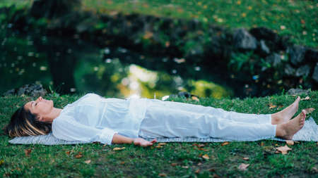 Corpse Position, Savasana, Meditation. Young woman practicing yoga and meditating by the water.の写真素材