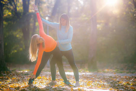 Women Stretching with Personal Fitness Trainer After Training in The Park.