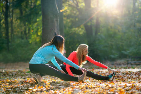 Women Stretching with Personal Fitness Trainer After Training in The Park.の写真素材