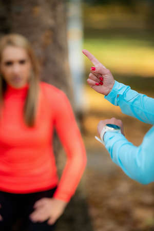 Women Exercising Outdoors in Public Park in the Fall. Trainer Looking at Woman Doing Squat Hold.の写真素材