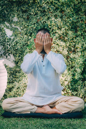A man sitting with his eyes closed and doing Reiki self-treatment. Reiki Practitioner holding hands on eyes.の写真素材