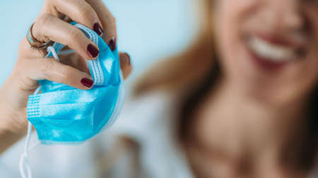 Smiling woman crumpling and throwing away a protective covid face mask. End of coronavirus pandemic concept.の写真素材