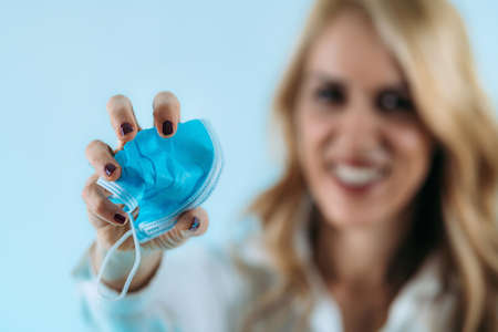 Smiling woman crumpling and throwing away a protective covid face mask. End of coronavirus pandemic concept.の写真素材