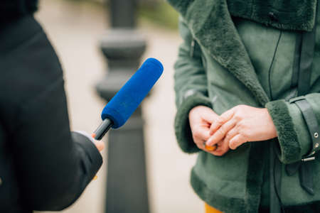 Journalist making an interview, holding a microphone, interviewing an unrecognizable male speaker.