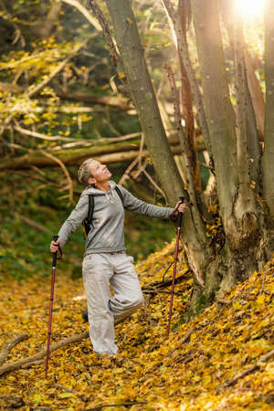 Mindful forest hike. Sporty middle-aged woman, hiking the forest trails, enjoying her surroundings on a beautiful autumn day, feeling harmony with natureの写真素材