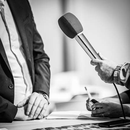 Journalists holding microphone, interviewing speaker.