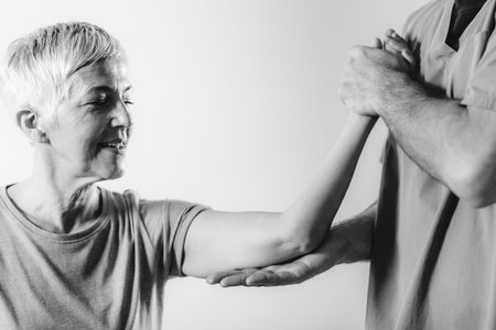 Therapist Checking Senior Womanâs Arm in Physical Therapy Officeの写真素材