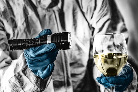 Police Crime Scene Investigator Examining Wine Glass with Forensic Light, Looking for Criminal Evidence.の写真素材