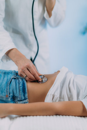 Pediatrician gastroenterologist, medical doctor who specializes in the diagnosis and treatment of gastrointestinal tract disorders doing abdominal examination with stethoscopeの写真素材