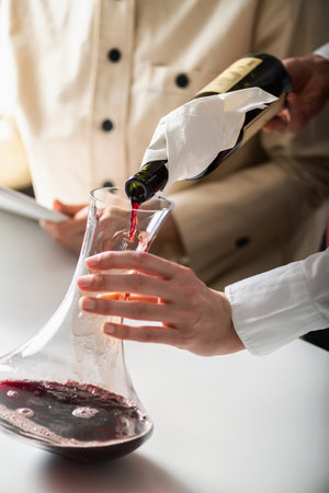 Decanting wine. A sommelier pours red wine from a bottle into a decanter, while explaining how to aerate wine to improve its flavor and aroma.の写真素材