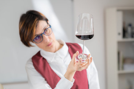 Sommelier holds a wineglass and evaluates the appearance of a red wine, looking at its color, clarity, and viscosity.の写真素材