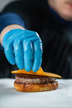Restaurant chef placing slice of cheese onto the burger close upの写真素材