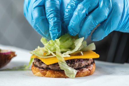 Restaurant chef placing chopped lettuce onto a burger, close upの写真素材