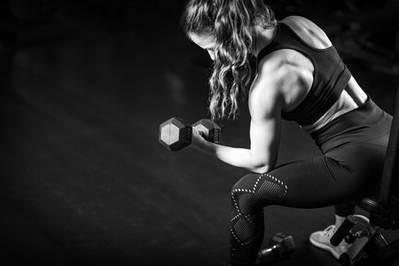 Female Athlete Exercising with Dumbbells in the Gym.
