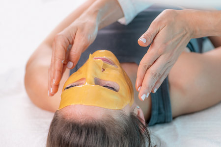 Dermatologist applies a yellow face mask for a rejuvenating beauty treatment. The mask helps to cleanse pores, brighten skin and healthy glow.の写真素材