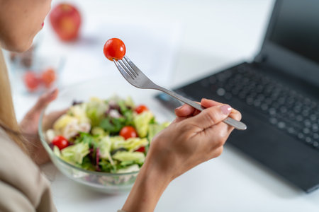 Healthy eating at work. Woman indulges in a delightful fresh salad at her workplace. With every bite, she embraces the nourishing flavors and invigorating energy of her nutritious meal, fueling her day with a refreshing and health-conscious choiceの写真素材