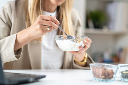 Nutritious meal at work. Woman indulges in a satisfying bowl of muesli and creamy yogurt, fueling her body with a balanced and energizing breakfastの写真素材