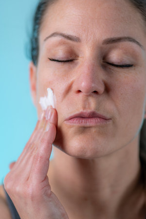 Taking care of skin with an at-home dermatology treatment. Woman applies cream to her skin, taking control of their own skincare routine.の写真素材