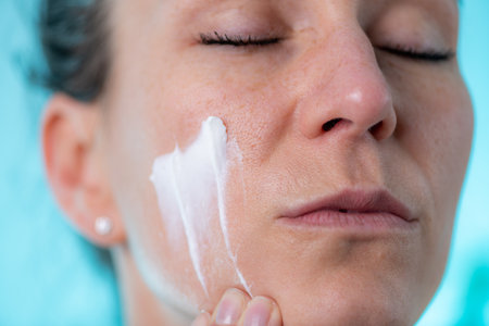 Taking care of skin with an at-home dermatology treatment. Woman applies cream to her skin, taking...