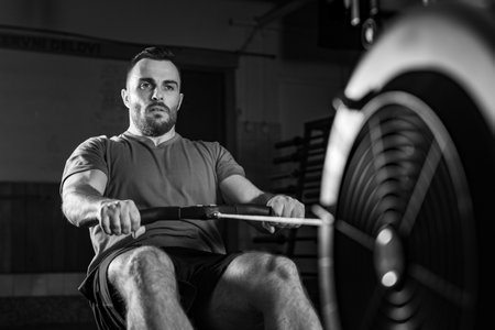 Young man excelling in a rowing machine exercise during cross training, dynamic black and white...