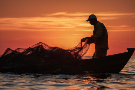 Silhouette of a fisherman holding empty nets against the warm hues of a setting sunの素材
