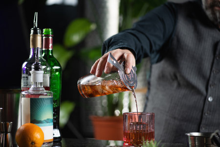 Skilled bartender pours Negroni cocktail through a cocktail drink strainer.