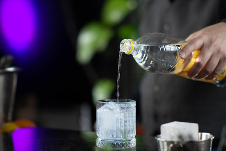 Bartender's hands pouring high quality tonic, preparing gin tonic cocktail.