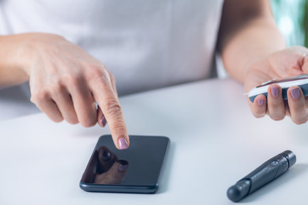 A woman tracks glucose levels and inputs data via smartphone, vital for diabetes management and...