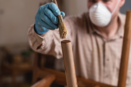 Carpenter wearing safety equipment applying clear wood stain on furnitureの写真素材