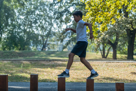 Young boy participates in outdoor physical activity, balancing on wooden stumps. Engaging in this fun exercise, he builds coordination and strengthの写真素材