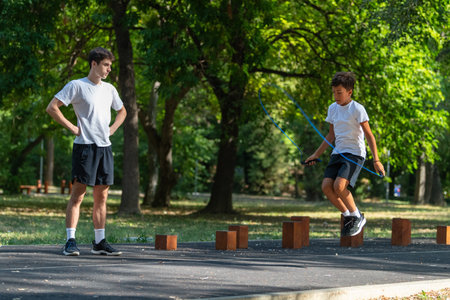 Boy practices jumping rope outdoors with a trainer, promoting fitness and coordination. This exercise session focuses on physical activity and improving agility in a fun outdoor environment.の写真素材
