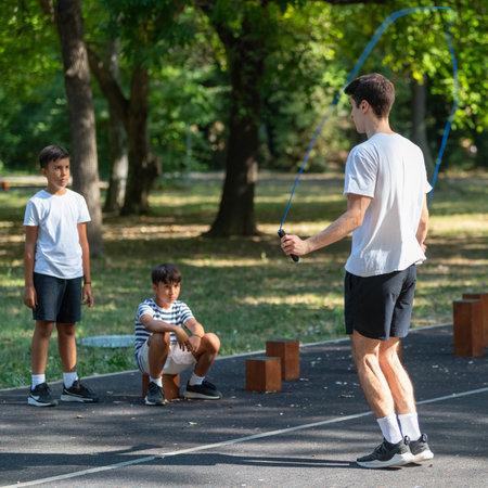 An outdoor fitness session where a trainer guides a children in jumping rope. This activity emphasizes building agility, coordination, and cardiovascular fitness in a fun, open air environment.の写真素材