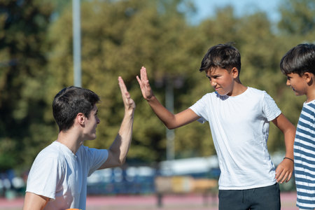 Coach and two young boys exchange a high five during outdoor basketball practice, capturing a moment...