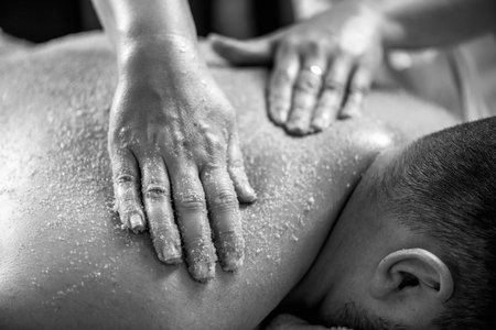 Scrubbing back massage, or massage with salts, combines exfoliation and relaxation to revitalize the skin and relieve tension in the back muscles. High contrast black and white photographyの写真素材