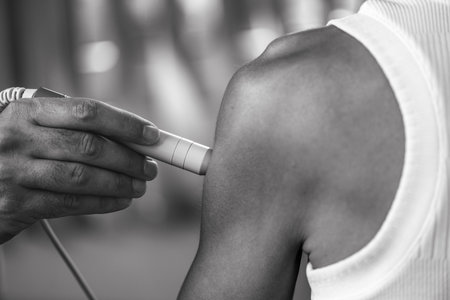 A physical therapist performs laser therapy on a patients shoulder to reduce pain, decrease...