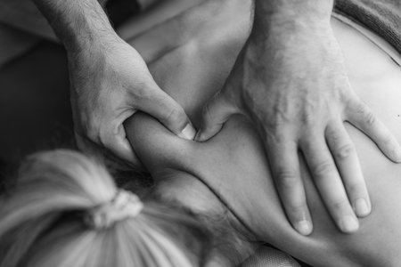 Physical therapist performs a deep tissue massage on a patients shoulder to relieve muscle tension and improve mobility in a therapeutic settingの写真素材
