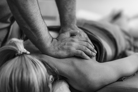 Physical therapist performs a deep tissue massage on a patients shoulder to relieve muscle tension and improve mobility in a therapeutic settingの写真素材