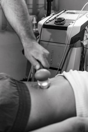 Physical therapist performs ultrasound therapy on a patient's lower back to alleviate pain and promote healing, enhancing mobility and recovery in a professional clinical settingの写真素材