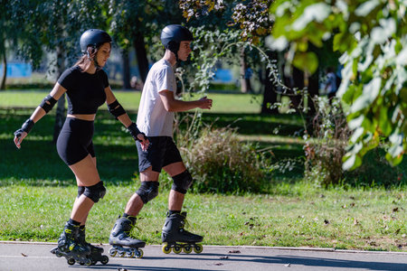 Young couple enjoys rollerblading on a sunny summer day in a lush park. The pair glides through...