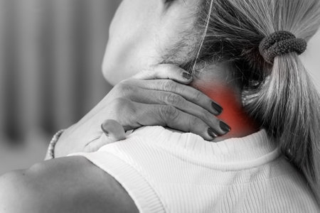 Woman experiencing neck pain, holding her sore neck with discomfort. The image highlights muscle strain, stiffness, or possible injury due to stress, poor posture, or prolonged screen use.の写真素材
